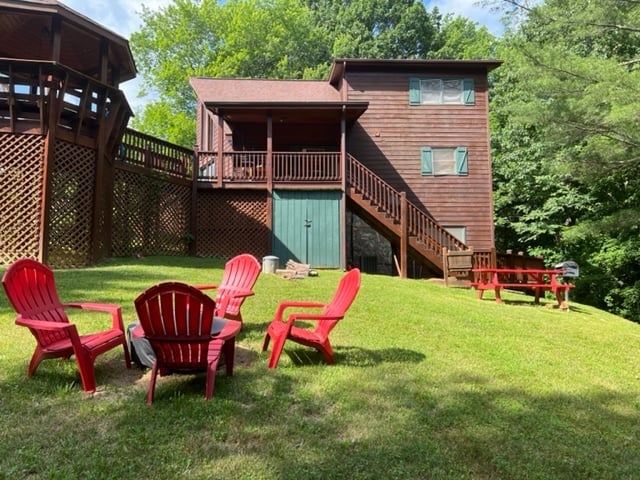 Red Adirondack chairs on green lawn in front of rustic wooden cabin with deck and surrounding trees