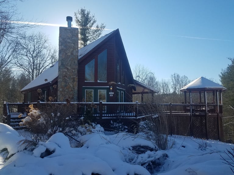 Modern red cabin with stone chimney surrounded by snow-covered landscape and bare trees on a clear winter day