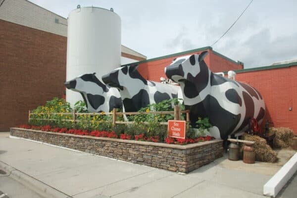 Giant cow sculpture with black and white spots in front of red brick industrial buildings with white water tower