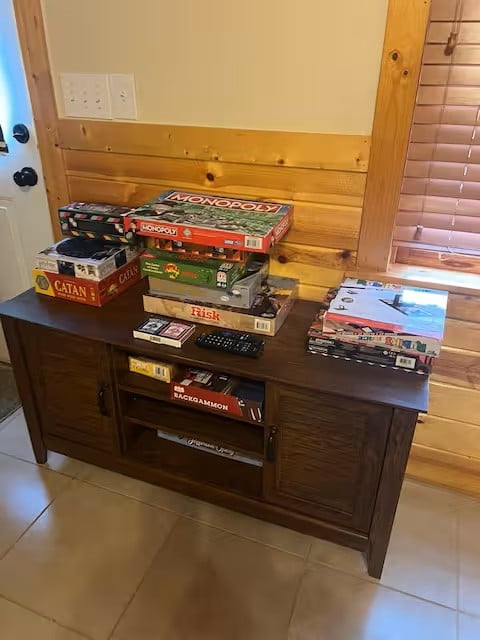 Dark wooden TV stand with shelves storing board games and media, including Monopoly and Catan boxes stacked on top surface