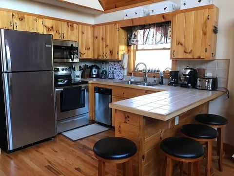 Rustic kitchen with wooden cabinets, stainless steel appliances, island with seating, and hardwood flooring