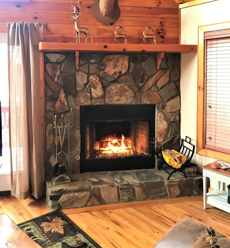 Stone fireplace with burning fire insert, wooden mantel decorated with deer figurines, fireplace tools, and accessories in rustic cabin interior