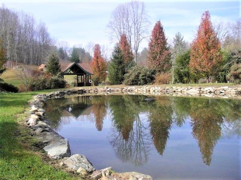 Scenic pond with gazebo reflecting colorful autumn trees and green lawn with stone-lined shores