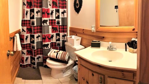 Rustic bathroom with wooden vanity, white sink, and moose-patterned red plaid shower curtain.