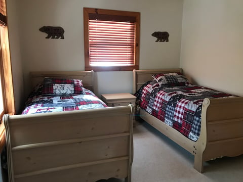 Two wooden twin beds with plaid bedding in a bedroom with bear silhouettes and red window blinds